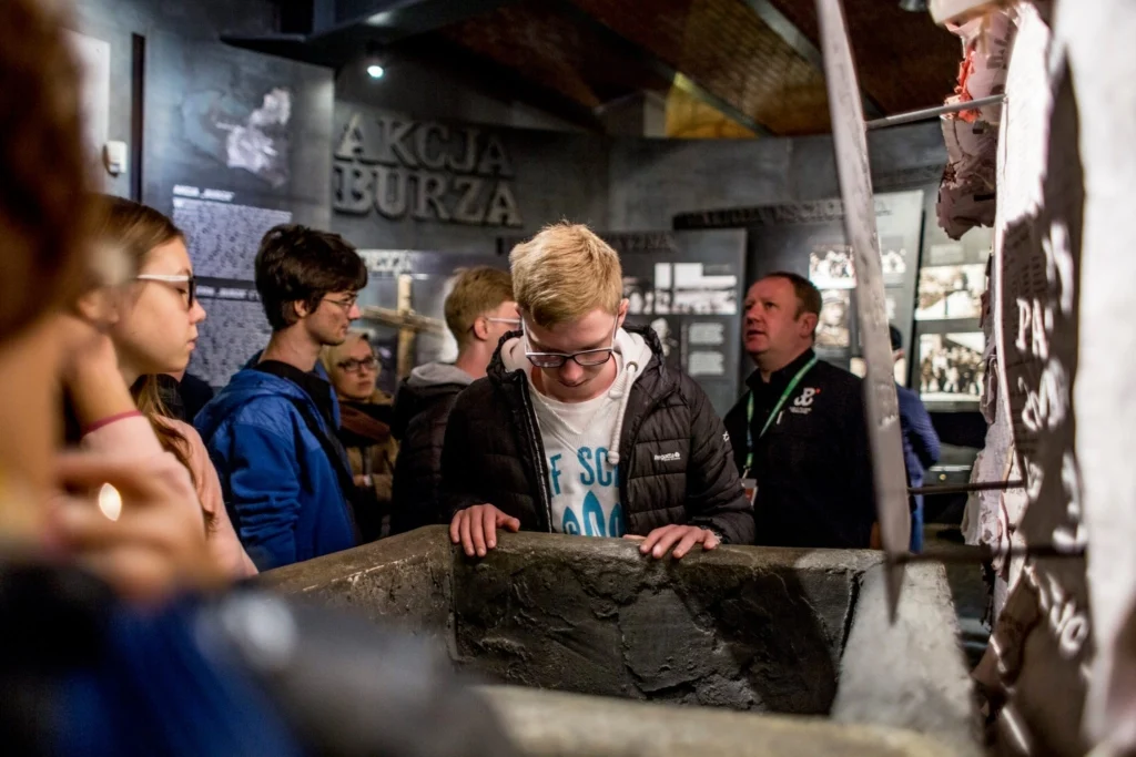 Grupa młodzieży zwiedza ekspozycję Muzeum Powstania Warszawskiego.