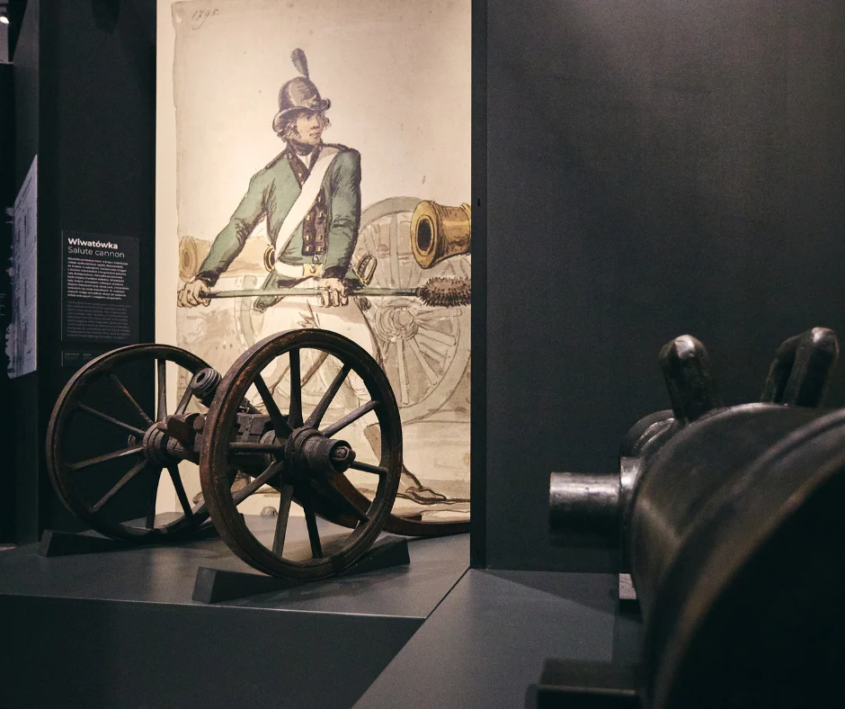 Wystawa czasowa w Muzeum Historii Polski. Na pierwszym planie armaty w tle wielkoformatowa grafika z żołnierzem.